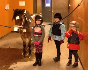 En häst och tre barn i stallet.